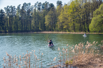 Beautiful scenery with lake and people paddling on a SUP, enjoying the day. Forest landscape in the background.