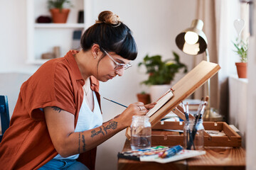 Artist, painting and woman with easel in home with creative inspiration at desk with project. Painter, working and sketch with brush on canvas in workshop with talent and skill in watercolor art