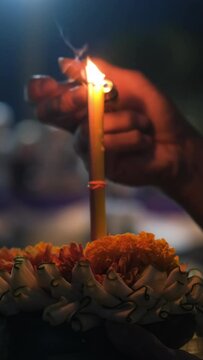 Vertical video. Close-up of hand of unrecognizible man lighting candle in Loy Krathong while praying to water goddess, selective focus