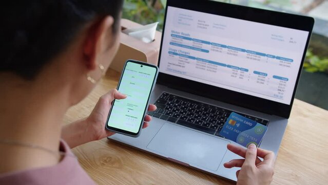 Over the shoulder view of woman filling online form with credit card sitting at desk in front of laptop