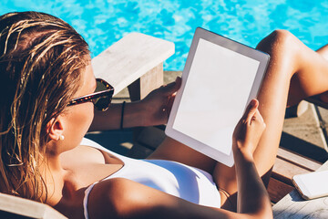 Female freelancer in sunglasses sunbathing on sunbed near blue pool and doing distance job online...