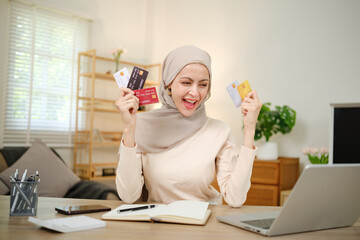 A woman is holding several credit cards and smiling. She is sitting at a desk with a laptop and a notebook