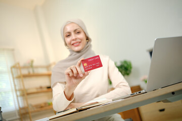 A woman is holding a red credit card in front of a laptop. She is smiling and she is happy