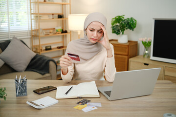 A woman is sitting at a desk with a laptop and a stack of credit cards. She is looking at the cards...