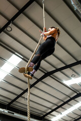 A middle-aged woman is working out inside a gym in sportswear.The 40-year-old is climbing a rope to...