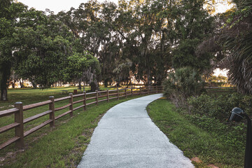 Paved path in the park with spanish moss trees and a wooden fence