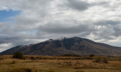 Vast field covered in dry grass and majestic mountain in the background The mountain’s slopes are dark and rugged, with patches of snow adorning its peak. Caucasian Mountains, Armenia