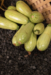 A basket full of green squash. The squash are piled on top of each other. The basket is made of wood