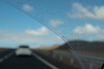 A car is driving down a road with a clear blue sky in the background. The windshield is covered in...