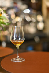 Single glass of white wine stands oncounter, with blurred background of bottles and bar atmosphere