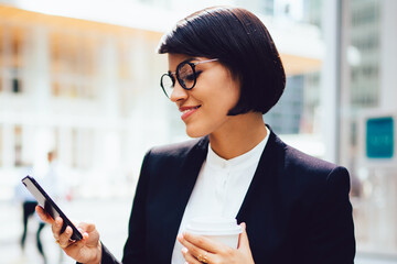 Successful female entrepreneur with tasty coffee in hands checking email on smartphone via high...