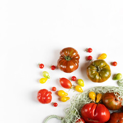 Red, green, yellow and striped tomatoes in string bag on gray table with space for text. Healthy food, fresh healthy vegetables from the garden