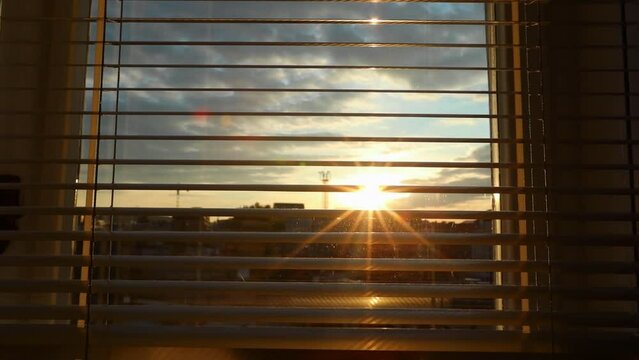 The sun's rays shine through the opening blinds