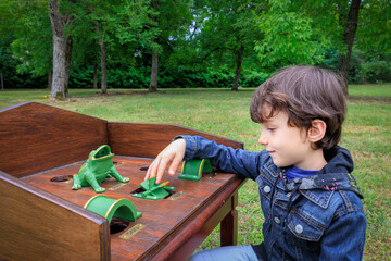 Young boy enjoying the Gioco della Rana table game outdoors. The child is focused on playing,...