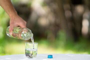 close up of male hand pouring water from bottle into glass, pouring glass of water, bottle of glass water filling copy space