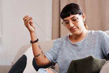 Woman, hands and embroidery on sofa for stitching fabric patch with needle on sweater at home....