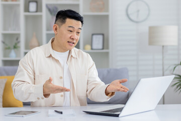 Man in casual wear gesturing while having an online meeting on a laptop at home. Modern interior...