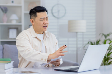 Fototapeta premium Middle-aged man on a video conference call while working from home office, using a laptop, tablet, and books.