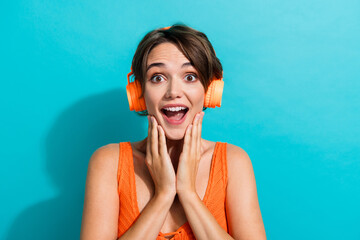 Photo of impressed woman dressed knitwear singlet in headphones astonished staring palms on cheeks isolated on turquoise color background