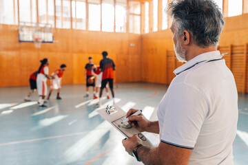 Mature male coach drawing game tactics using a coach clipboard during practice
