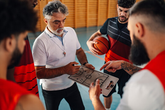 Mature basketball coach and his diverse team having a team talk during practice