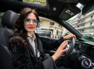 Beautiful black haired sexy girl in dark glasses driving a car.