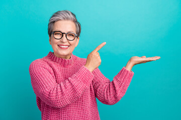 Photo of toothy beaming person dressed knit sweater in eyewear indicating at object on arm empty...