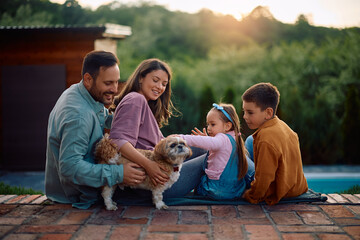 Happy family relaxing with their dog in backyard at sunset.