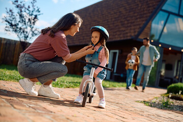 Happy mother assisting her small daughter in riding  bicycle outdoors.