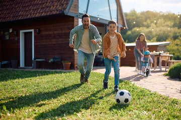 Happy father and son playing soccer in backyard.