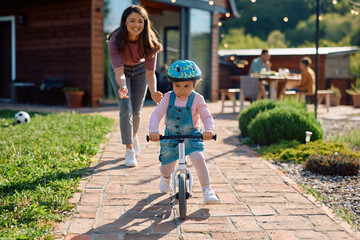 Little girl learning to ride bicycle with help of her mother.