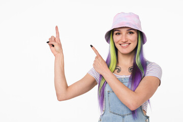 Cheerful caucasian hipster young girl woman with dyed colorful hair in cap pointing showing copy space free space isolated in white background