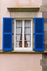 Blue shuttered window on a pink stuccoed building.