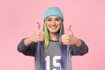 Closeup cropped portrait of positive teenage girl woman hipster with dyed colorful hair smiling with toothy smile showing thumbs up likes isolated in pink background