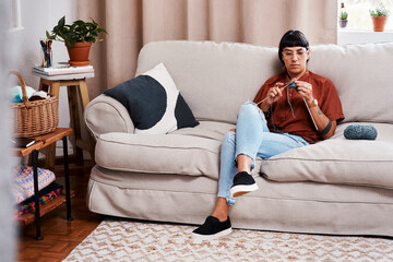 Woman, knitting and relax with wool in home or creative project on sofa with stitching pattern....