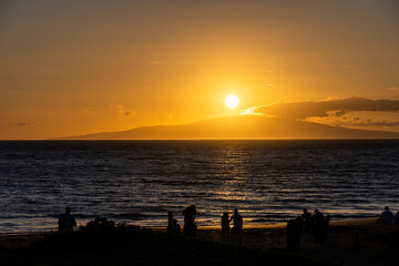 Silhouettes of people watching the warm sunset over the Pacific Ocean from the beach at Kihei, Maui, Hawaii, as a nature background
