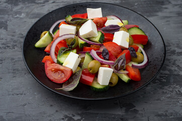 Greek salad on a black plate on a dark background. Horizontal..