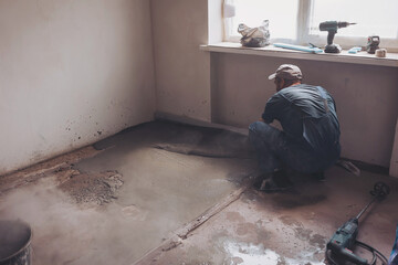 Male construction worker using screed rail while screeding floor in living room. Man flattening and...