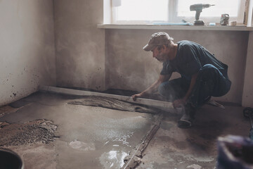 Male construction worker using screed rail while screeding floor in living room. Man flattening and...
