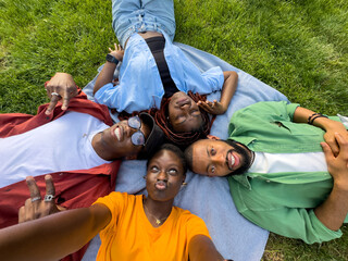 Happy group of african american friends girls and guys fool around, resting on grass, make selfie...