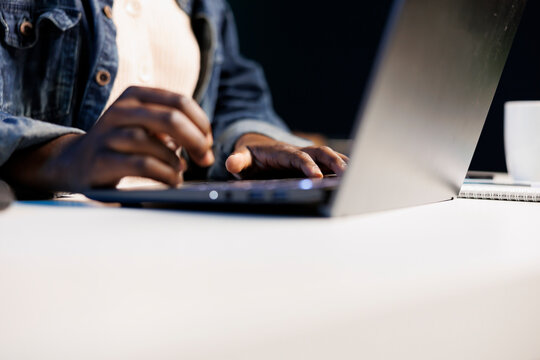 Close up of black person utilizing modern technology by typing on portable computer. Selective focus on hands of african american individual taking notes on laptop and surfing the net.