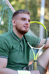 Young happy handsome man in polo play tennis outdoors with tennis racket on court at summer day