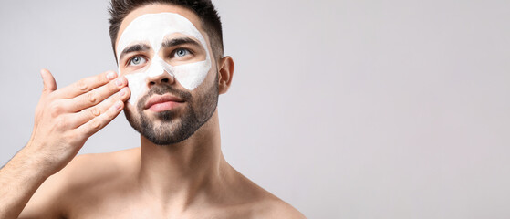 Handsome man with clay mask on his face against light background