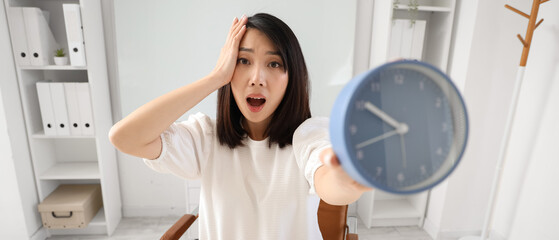 Shocked Asian woman with alarm clock in office