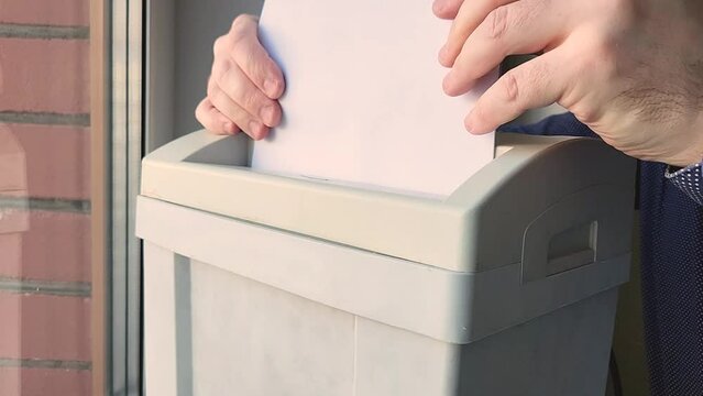 man's hands inserts old documents into a shredder for shredding