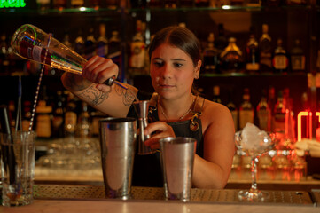 Young woman barman preparing cocktail and pouring it into glass.