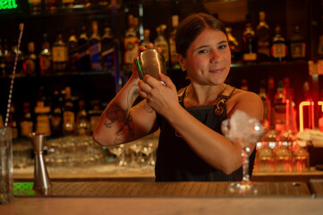 Young woman barman preparing cocktail and pouring it into glass.