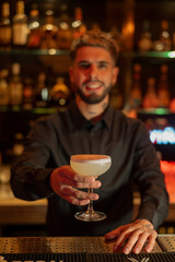 Young elegant barman working behind a bar counter mixing drinks