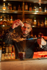 Young elegant barman working behind a bar counter mixing drinks