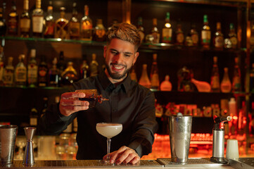 Young elegant barman working behind a bar counter mixing drinks